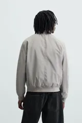 Cazadora bomber ligera gris confeccionada en tejido técnico. Cuello y puños en rib elástico, manga larga, bolsillos de vivo en cadera y bolsillo interior. Cierre frontal con cremallera.