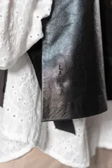 Chaleco corto negro de cuero con solapas y bolsillos frontales.