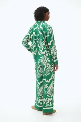 Camisa de manga larga verde con estampado de hojas blancas. Tiene cuello clásico, cierre con botones y puños con botón.