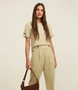 Pantalón zanahoria de cintura alta color beige, confeccionado en tejido piqué con viscosa sostenible. Cuenta con cierre tradicional, cintas con botones en la cintura, pliegues y dobladillo en el bajo.