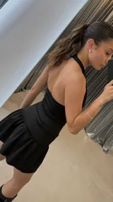 Vestido corto negro con escote halter, abertura circular en el pecho y falda con volados.