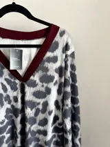 Sweater de punto con cuello en V y estampado animal print en tonos grises y blancos. Tiene ribete marrón en el cuello, puños y bajo elastizados.