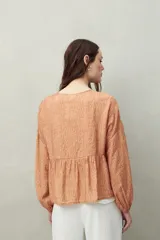 Blusa estampada celeste y blanca de caída fluida con cuello redondo y lazos frontales. Diseño con cortes horizontales y frunces, mangas largas con puños elastizados.
