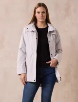 Campera impermeable color gris claro, marca Gallery. Tiene abertura central con cierre oculto y botones a presión, bolsillos delanteros y capucha plegable en el cuello.