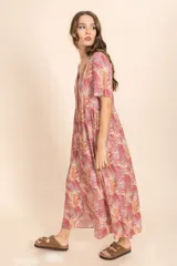 Vestido largo color ladrillo con estampado de hojas en tonos blanco y amarillo. Tiene escote en V, mangas cortas y botones frontales.