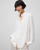 Camisa blanca de poliéster con cuello alto, frunce en el escote, manga larga con puño y pliegue central en la espalda.