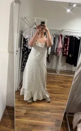 Vestido largo de algodón color blanco con estampado de lunares pequeños en color marrón. Presenta tirantes finos y escote pronunciado en la espalda. El ruedo tiene un volante con fruncido.