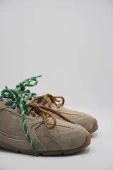 Zapatillas urbanas color marrón claro, confeccionadas en cuero, con cordones verdes y suela de goma.