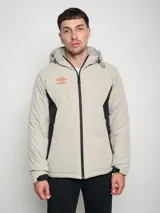 Campera corta Umbro Crafted Pro color beige con paneles laterales negros y logo Umbro naranja en el pecho.