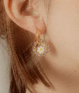 Aros colgantes con forma circular, con strass y dije de resina transparente con una flor blanca de vidrio en el interior. El arito es de acero quirúrgico dorado.
