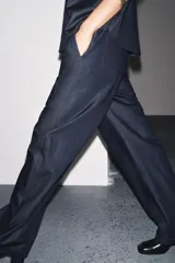 Pantalón de denim azul oscuro, de tiro medio y corte ancho, con cintura elástica en la parte trasera y cierre frontal con cremallera y botón.