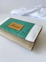 Billetera de cuero turquesa, blanco y beige con diseño texturizado. Tiene sistema de cierre con broche y monedero externo.