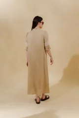 Vestido largo color beige, confeccionado en lino, con escote en V con volados y apliques de puntilla en las mangas. Posee bolsillos delanteros y tajos laterales.