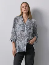 Camisa de mujer estampada con hojas en blanco y negro, cuello con solapa, abertura central con botones, bolsillos aplicados en el delantero y mangas largas con lazo.