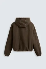 Cazadora relaxed fit confeccionada en tejido de algodón denim color marrón. Cuello con capucha ajustable y manga larga. Bolsillos frontales tipo canguro. Acabados con elástico. Efecto lavado. Cierre frontal de cremallera.
