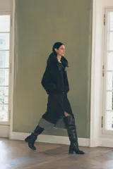 Chaqueta negra de cuello redondo confeccionada en hilatura con 50% lana. Tiene capucha extraíble, manga larga con puño interior, bolsillos delanteros y bajo ajustable con cordón elástico. Cierre frontal con cremallera metálica.