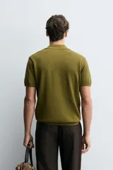 Jersey de punto color verde oliva, de calce relajado (relaxed fit), con cuello solapa y abertura frontal en forma de V. Es de manga corta y presenta acabados en rib en puños y ruedo.