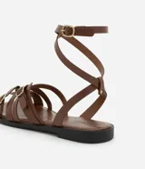 Sandalias planas de cuero color marrón, con múltiples tiras finas ajustables con hebillas doradas. Tira que se ata al tobillo.