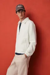 Campera blanca de denim rígido con cuello clásico, cierre frontal con cremallera, bolsillos laterales y un bolsillo interior. Tiene elástico en puños y bajo. Corte estándar y forro interior.