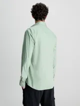 Camisa verde claro de popelín elástico, corte slim, con cierre frontal de botones, mangas largas y logo de Calvin Klein bordado en el pecho.