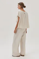 Blusa color crema de lino metalizado, de calce recto, con cuello bote y mangas cortas.