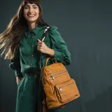 Mochila de símil cuero color marrón con apertura superior y tres bolsillos frontales con cierres metálicos. Cuenta con bolsillos laterales, compartimentos internos y una correa de galón regulable con diseño geométrico para utilizar como bandolera.