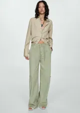 Camisa color beige de corte crop, confeccionada en mezcla de lino y lyocell. Tiene cuello camisero, cierre frontal con botones, manga larga con puños abotonados y lazo ajustable en la cintura.