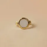 Anillo de plata 925 con baño de oro, engaste circular con piedra central de nácar blanco. El aro tiene detalles estriados en el engaste.