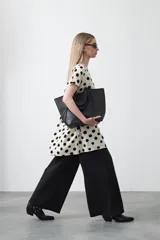 Vestido corto de silueta amplia con corte bajo busto, cuello a la base y mangas cortas. El tejido presenta un estampado de hojas en tonos rojo óxido y turquesa sobre un fondo de rayas verticales blancas y negras.