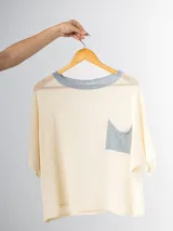 Remera tejida en hilo italiano, color beige, con cuello a la base y bolsillo frontal. De caída relajada y silueta amplia.