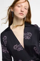 Vestido largo estilo camisero confeccionado en seda viscosa color negro con estampado de tigres en color rosa. Tiene cuello camisero, mangas largas, corte cruzado y lazo en la cintura.