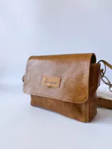 Bandolera color camel de cuero con forro de tela, correa corta con tientos y bolsillo interno.