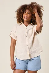 Camisa color beige claro, de corte clásico, con cuello, botones frontales, bolsillo en el pecho y mangas tres cuartos con presilla para sujetar.