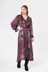 Vestido largo cruzado con estampado floral en tonos fucsia, negro, rojo y blanco. Tiene escote en V con volantes, mangas largas abullonadas y lazo para ajustar en la cintura.