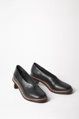 Zapato escotado liso de cuero caprino, con base de suela de goma y taco isla de madera torneada.
