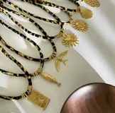 Gargantilla con cordón estampado animal print y dijes dorados con diferentes motivos: concha, sol, corazón, golondrina, pez y palmera.