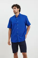 Camisa de manga corta azul con pequeños lunares blancos, cuello button-down y bolsillo en el pecho.