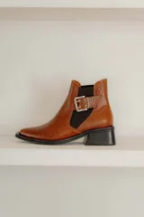 Botines Chelsea color beige con elásticos laterales negros, punta cuadrada, detalle de hebilla lateral y tacón bloque bajo.