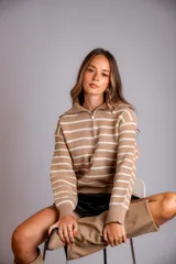 Sweater de punto color beige con rayas horizontales blancas, cuello polo con cierre de cremallera y mangas largas.