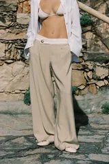 Pantalón color beige de tiro alto con cintura combinada en blanco, pinzas delanteras y pernera ancha. Cierre frontal con cremallera y botón.