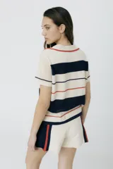 Remera polo tejida color crema con rayas horizontales en azul marino y rojo. Presenta cuello clásico, corte relajado y bordado de un ají rojo en el pecho.