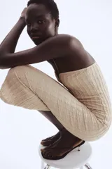 Vestido midi ajustado color beige, sin tirantes (strapless), con escote corazón que incluye un alambre de metal revestido para soporte y un borde de silicona oculto para mejor ajuste. El tejido presenta una textura plisada o arrugada vertical.