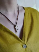 Gargantilla marrón de cuero con dije de bronce en forma de letra M.