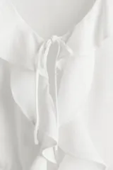 Blusa blanca entallada corta en tejido liviano de mezcla de lino y viscosa. Modelo de manga corta con escote redondo pronunciado, delantero abierto con tira fina doble y cordón para ajustar en la cintura. Volados anchos en escote, abertura, mangas y bajo.