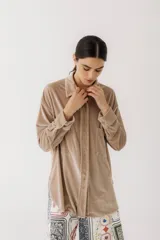 Camisa beige de terciopelo con cuello clásico, cierre frontal con botones, dos bolsillos de parche en el pecho y mangas largas con puños abotonados.