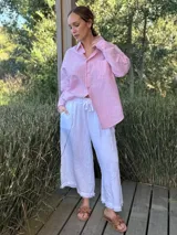 Camisa holgada a rayas verticales color beige y blanco, con cuello clásico, manga larga, bolsillo en el pecho y cierre frontal con botones nacarados.