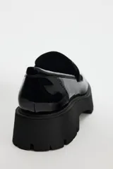 Zapato tipo mocasín negro acharolado con antifaz y suela track.