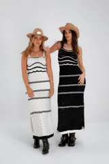 Vestido largo de punto calado blanco con rayas horizontales negras y breteles finos. El vestido tiene un corte recto y aberturas laterales en el ruedo. Las modelos llevan sombrero de estilo cowboy y botas de cuero.