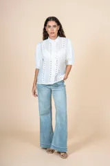 Blusa blanca con detalles bordados en toda la superficie, cuello levemente subido y botones al frente.