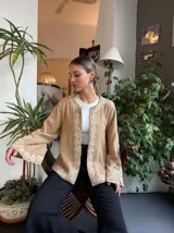 Campera color beige con bordado floral blanco en el frente, mangas y cuello. Tiene mangas largas acampanadas y corte recto.